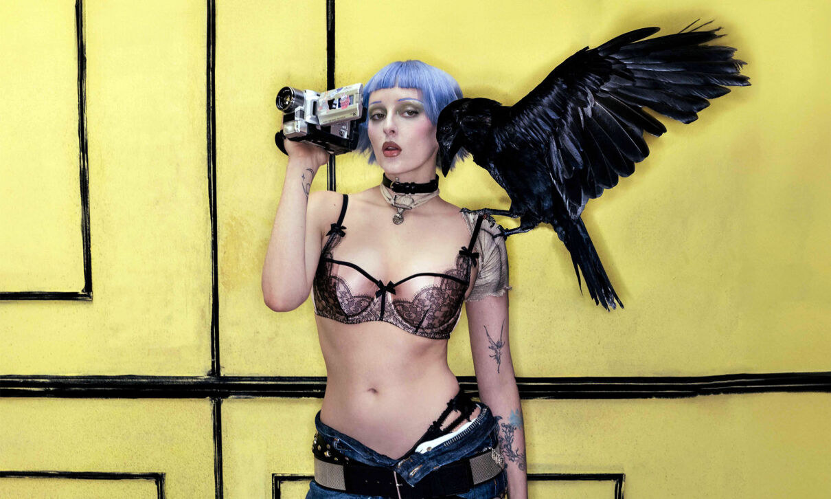 Die Sängerin Ashnikko mit Kamera in der Hand und einer Krähe auf der linken Schulter.