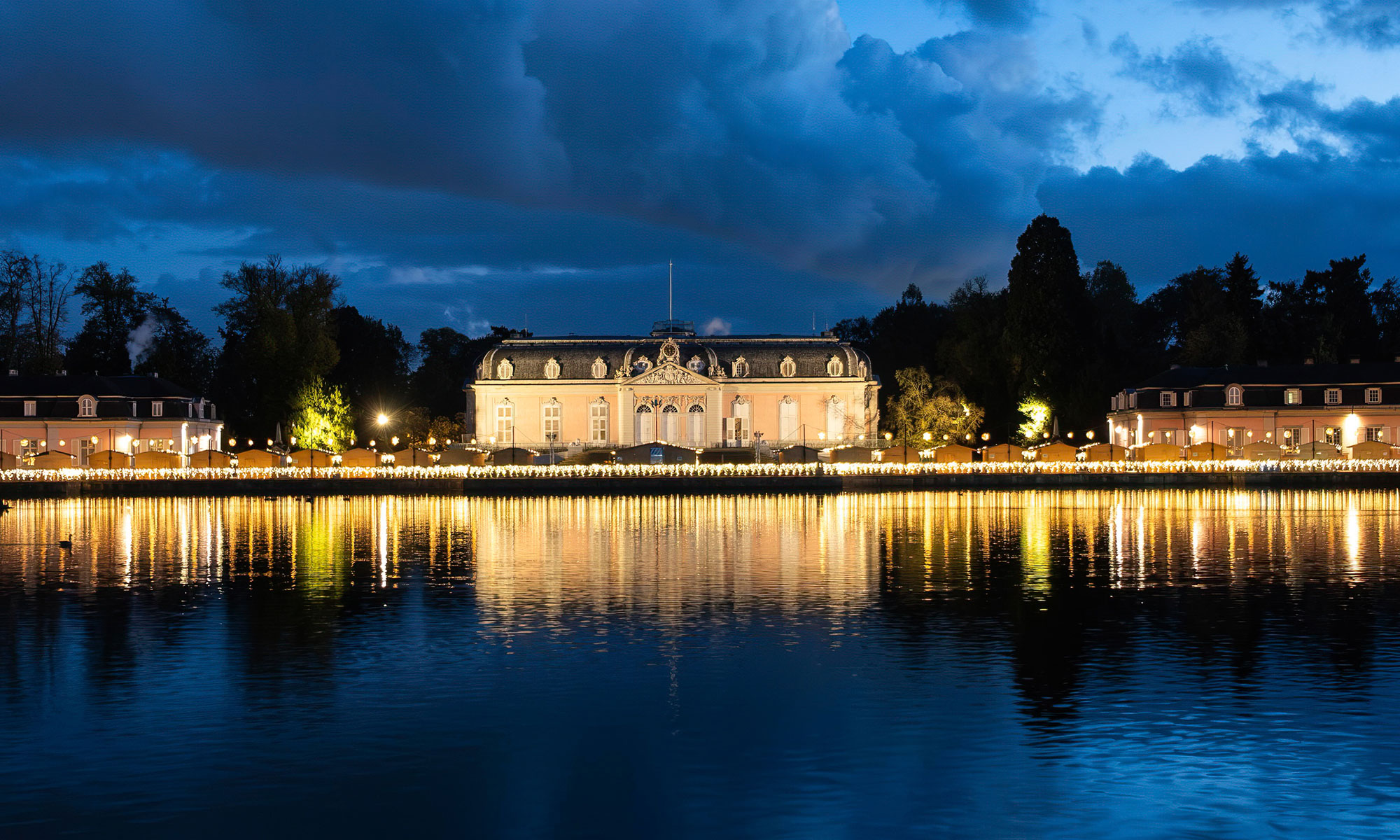 Schloss Benrath in der Dämmerung mit erleuchteten Weihnachtsmarkthütten