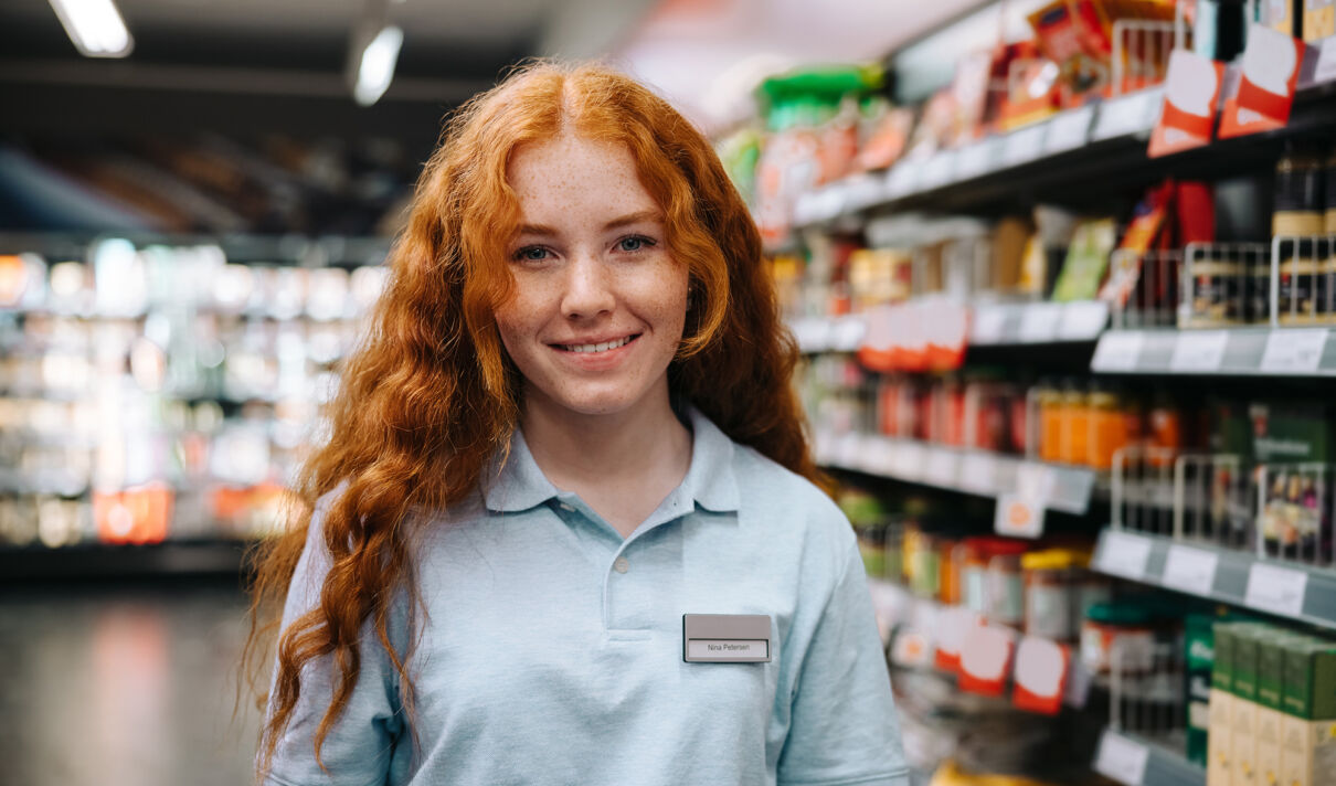 Ein junge Supermarkt-Mitarbeiterin steht vor Verkaufsregalen