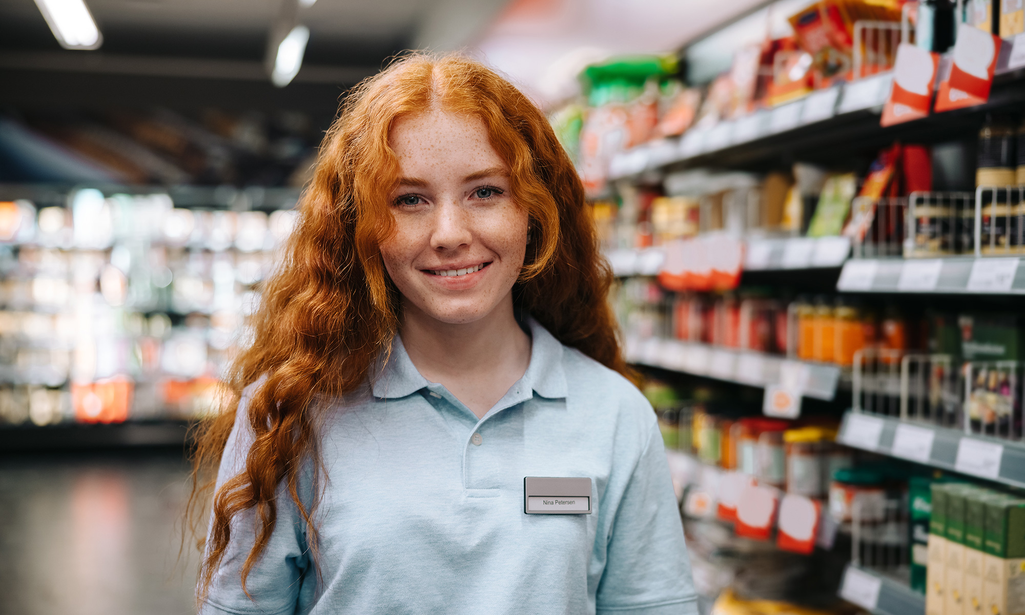 Ein junge Supermarkt-Mitarbeiterin steht vor Verkaufsregalen