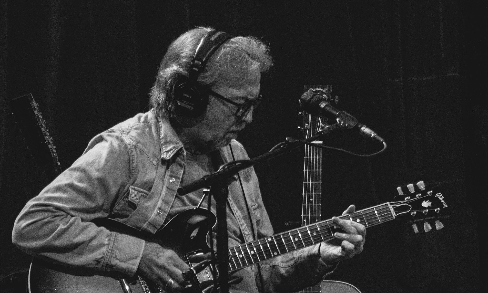 Eric Clapton mit Kopfhörern spielt Akustikgitarre in einem Tonstudio.