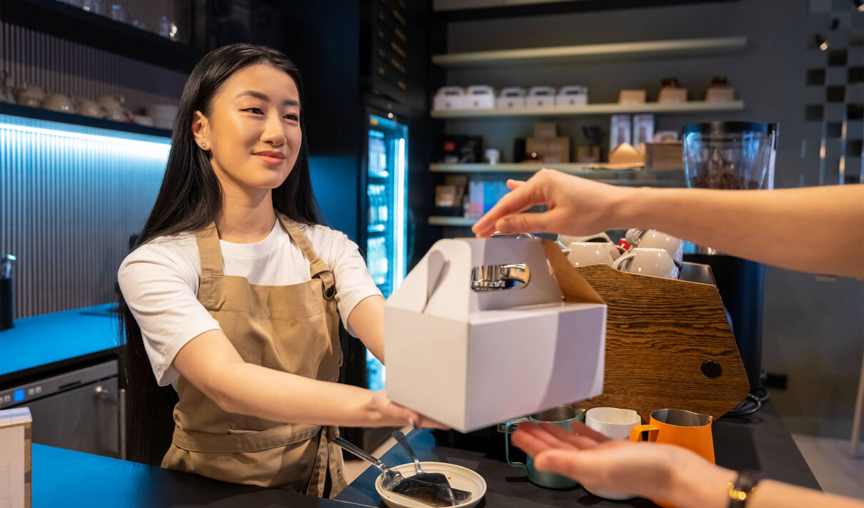 Eine Bedienung hinter der Theke eines Cafès reicht einem Kunden ein Paket