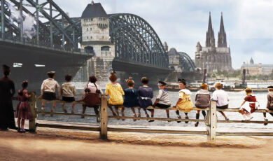 Ein altes Foto zeigt Kinder, die auf einem Geländer sitzen, mit Blick auf Hohenzollernbrücke und Dom.