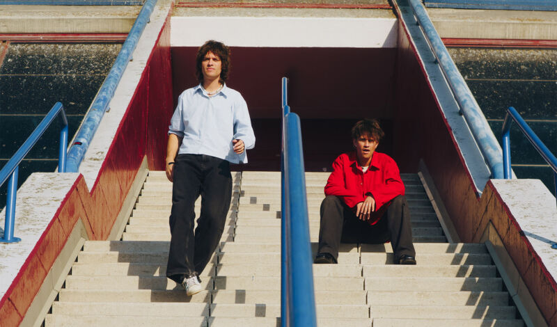 Henry und Pierre Beasley von der neuseeländischen Band Balu Brigada auf einer Treppe in einem Stadion.