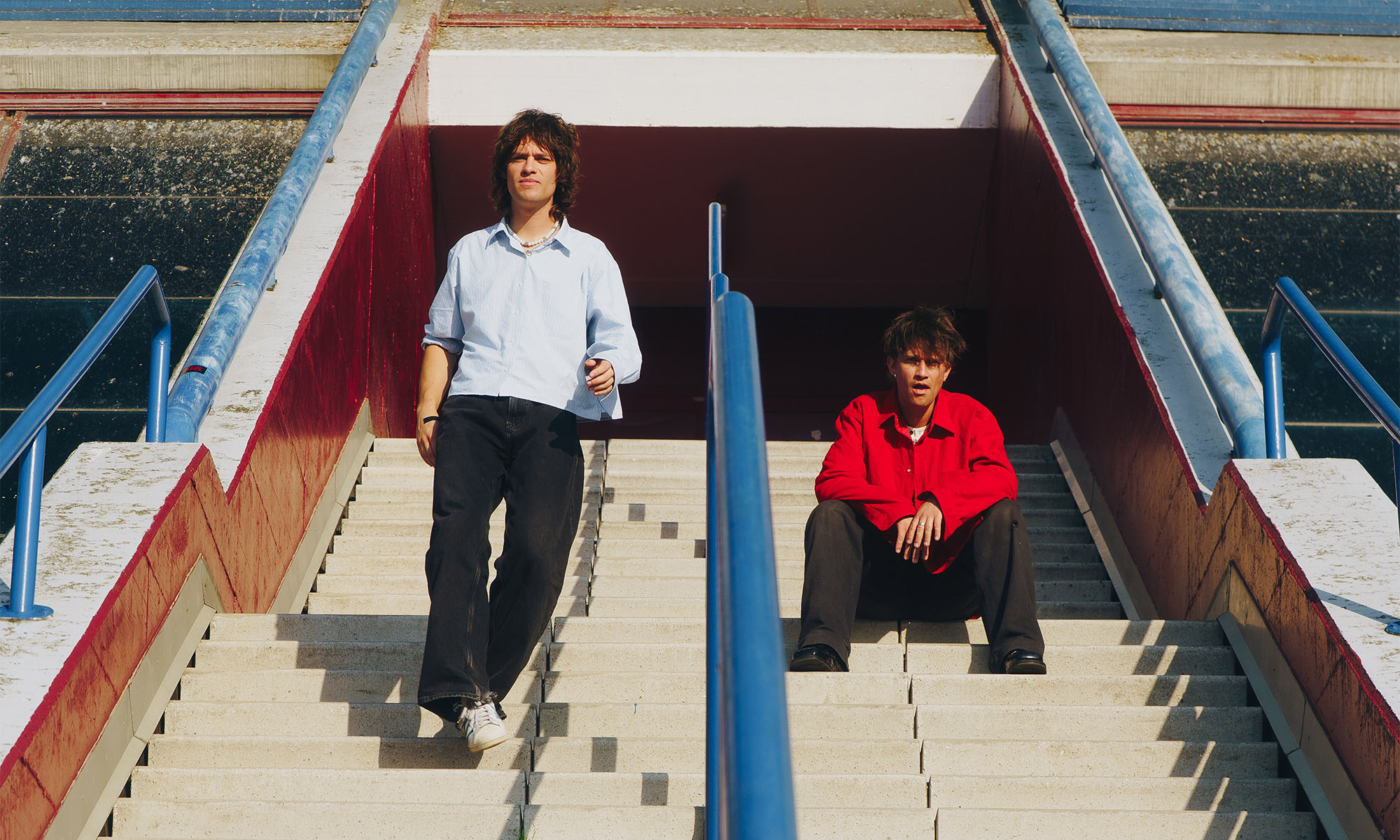 Henry und Pierre Beasley von der neuseeländischen Band Balu Brigada auf einer Treppe in einem Stadion.