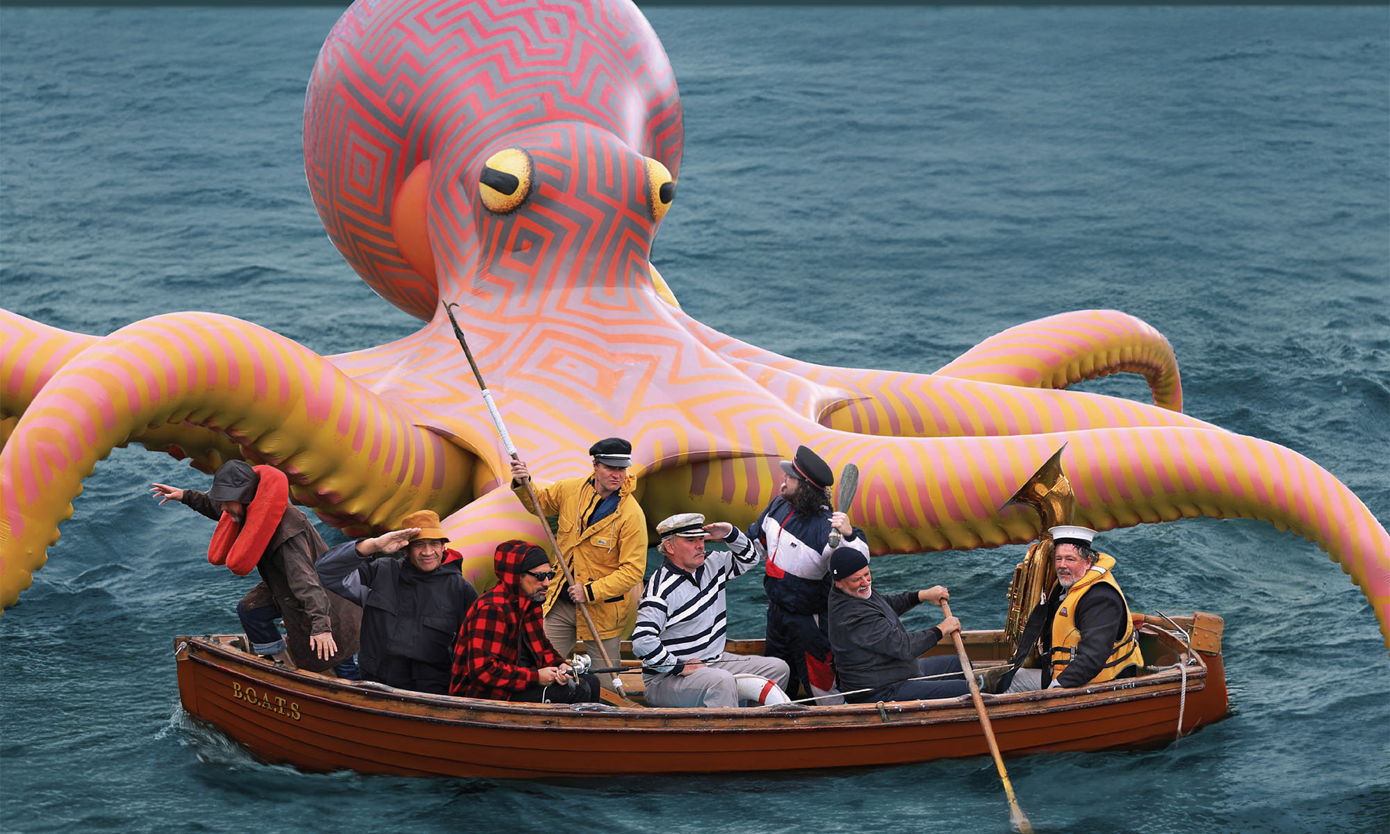 Die Musiker der Band Fat Freddys Drop sitzen in einem Ruderboot, im Hintergrund ist ein bunter riesiger Krake zu sehen.