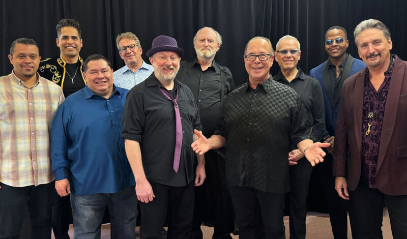 Die Musiker der Band Tower of Power stehen vor schwarzem Hintergrund.
