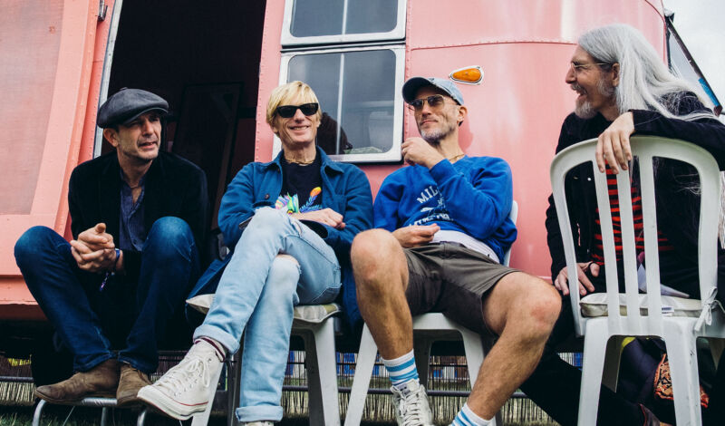 Die Musiker der Band Kula Shaker sitzen auf Plastikstühlen vor einem rosafarbenen Wohnwagen