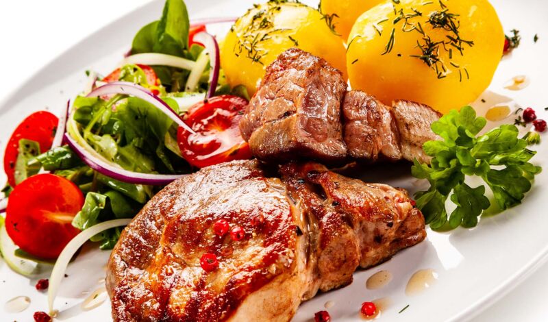 Auf einem weißen Teller sind zwei Koteletts mit kartoffeln und Salat angerichtet.