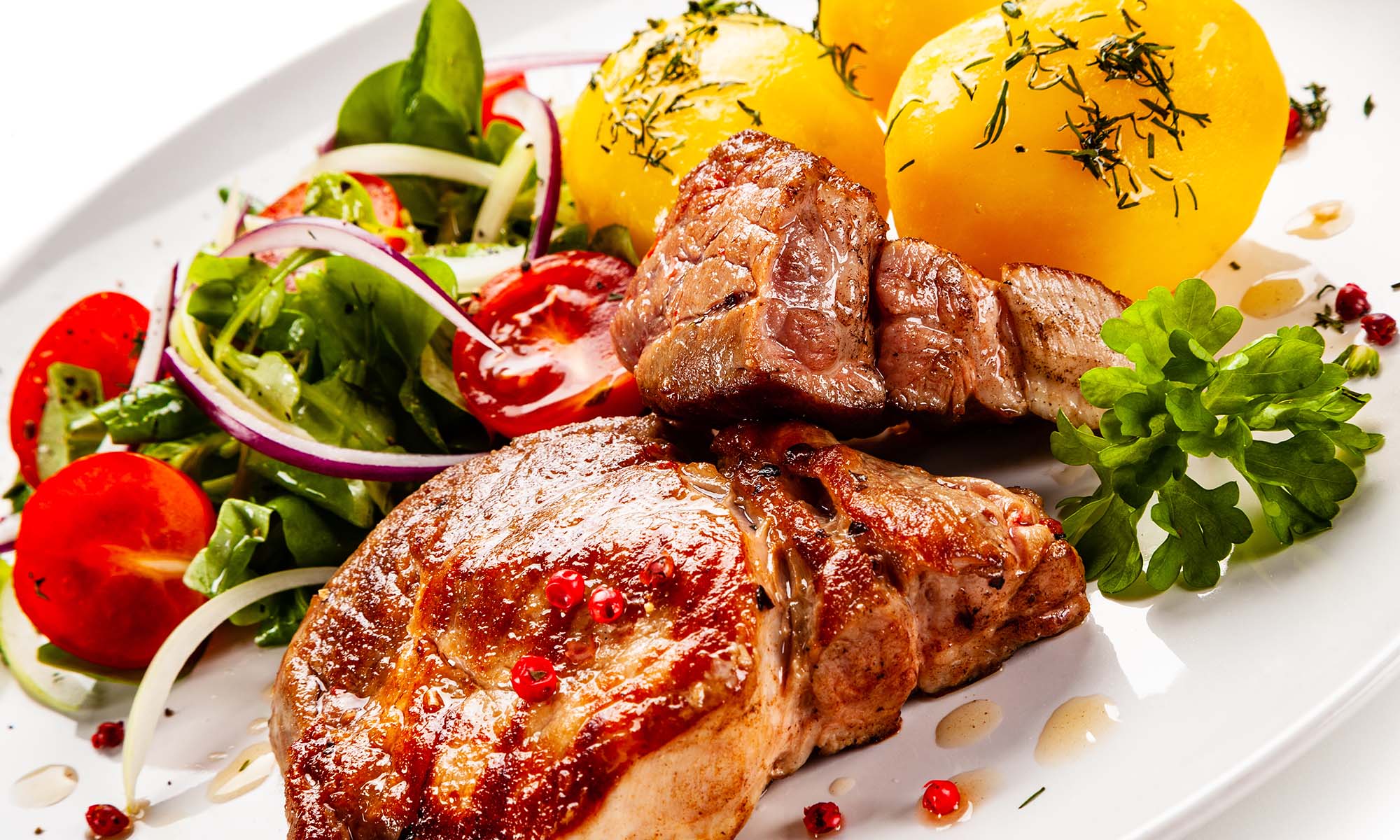 Auf einem weißen Teller sind zwei Koteletts mit kartoffeln und Salat angerichtet.