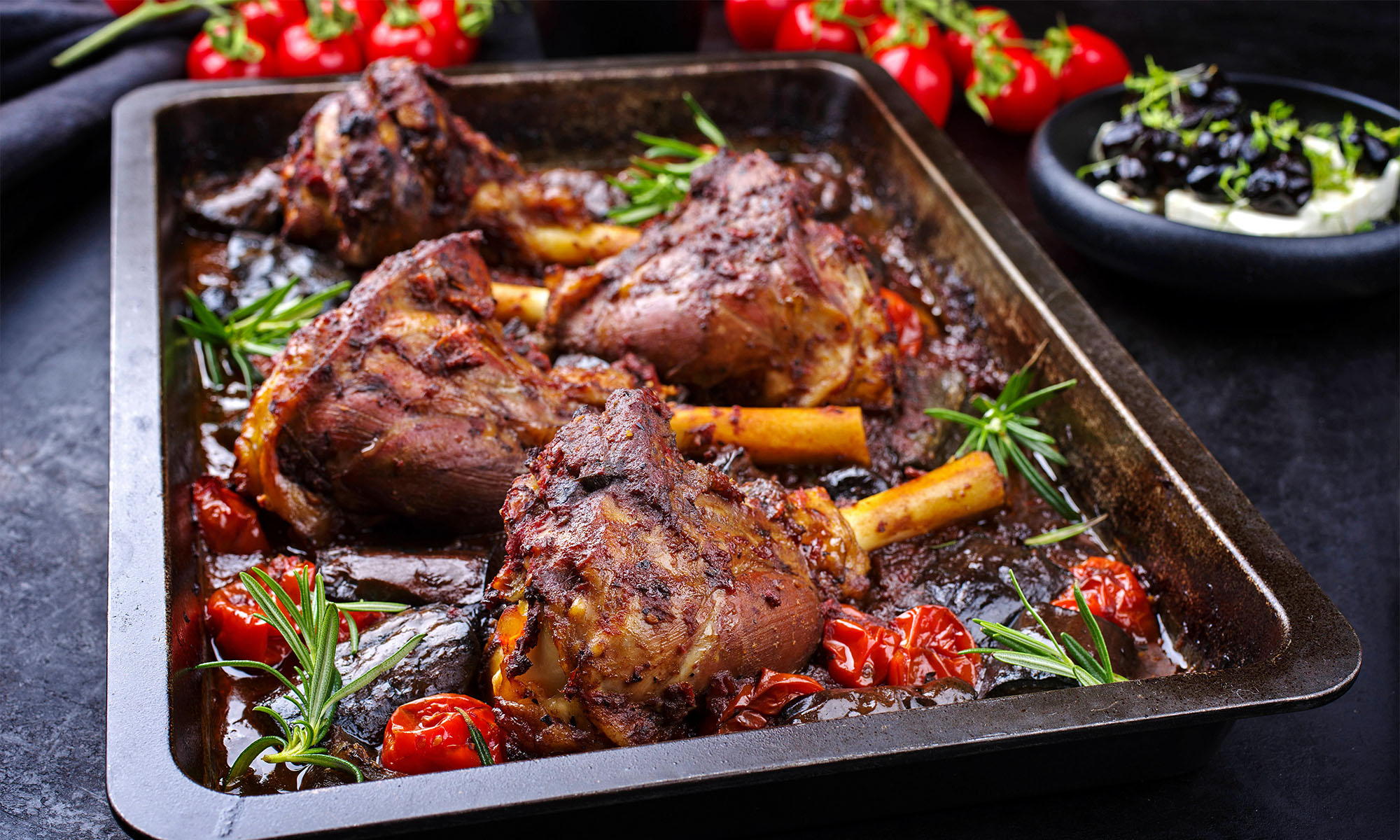 Mehrere gegrillte Lammhaxen mit Gemüse auf einem Backofenblech