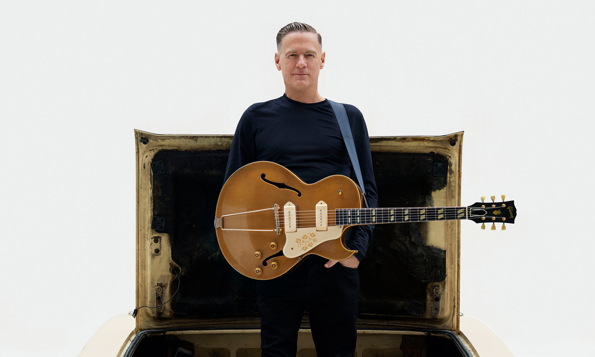 Bryan Adams mit einer Gitarre steht im Kofferaum eines Autos
