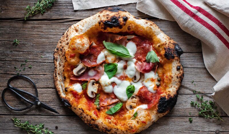 Eine Pizza Neapolitana mit breitem Rand und Tomate, Mozzarella und Basilikum