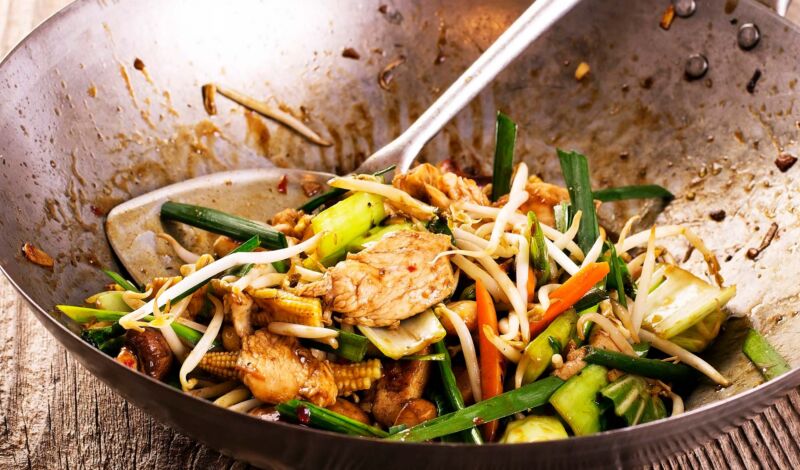 In einem Wok wird Gemüse zusammen mit Hähnchenfleisch gegart.