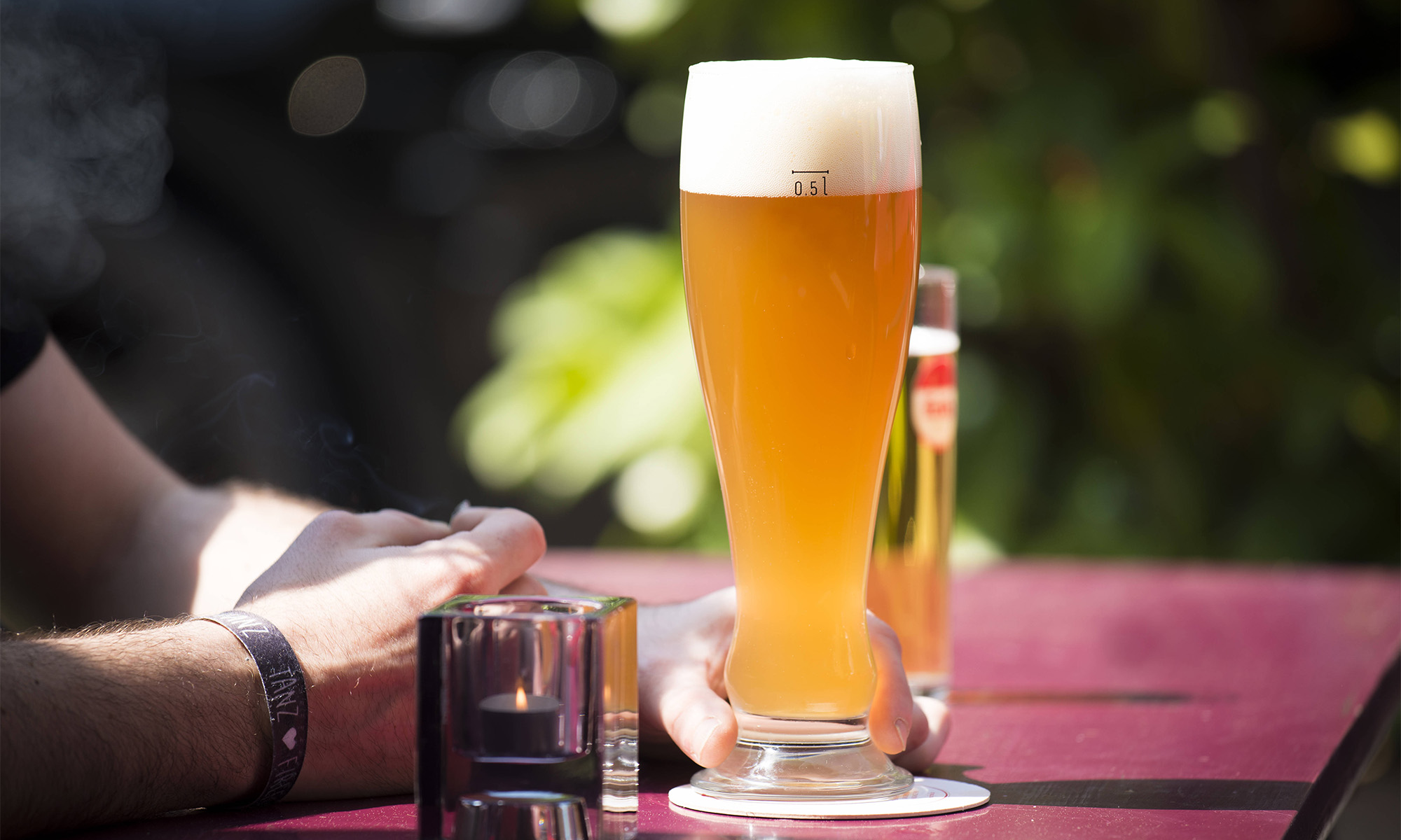 Ein Weizenbier steht auf einem Biertisch in einem Biergarten