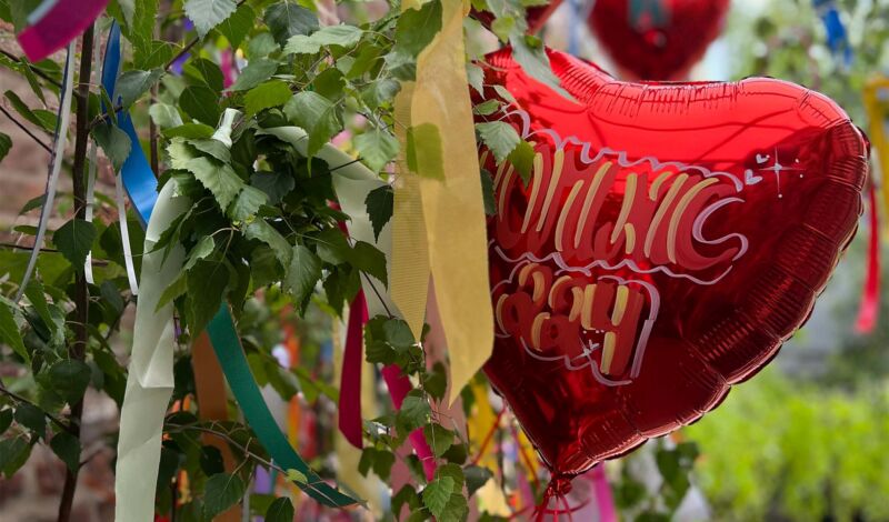 Ein roter Luftballon in Herzbaum mit Blättern einer Birke und buntem Kreppband