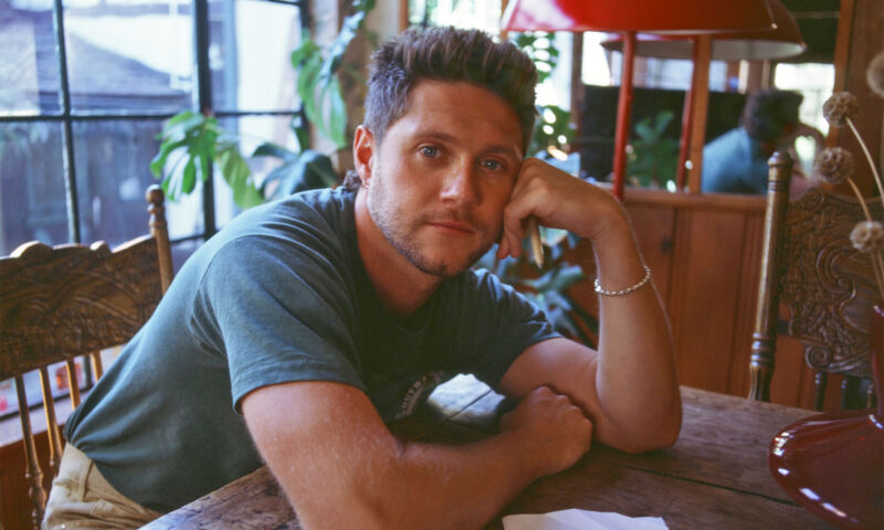 Der irische Sänger Niall Horan sitzt an einem Tisch, den Kopf auf eine Hand gestützt.