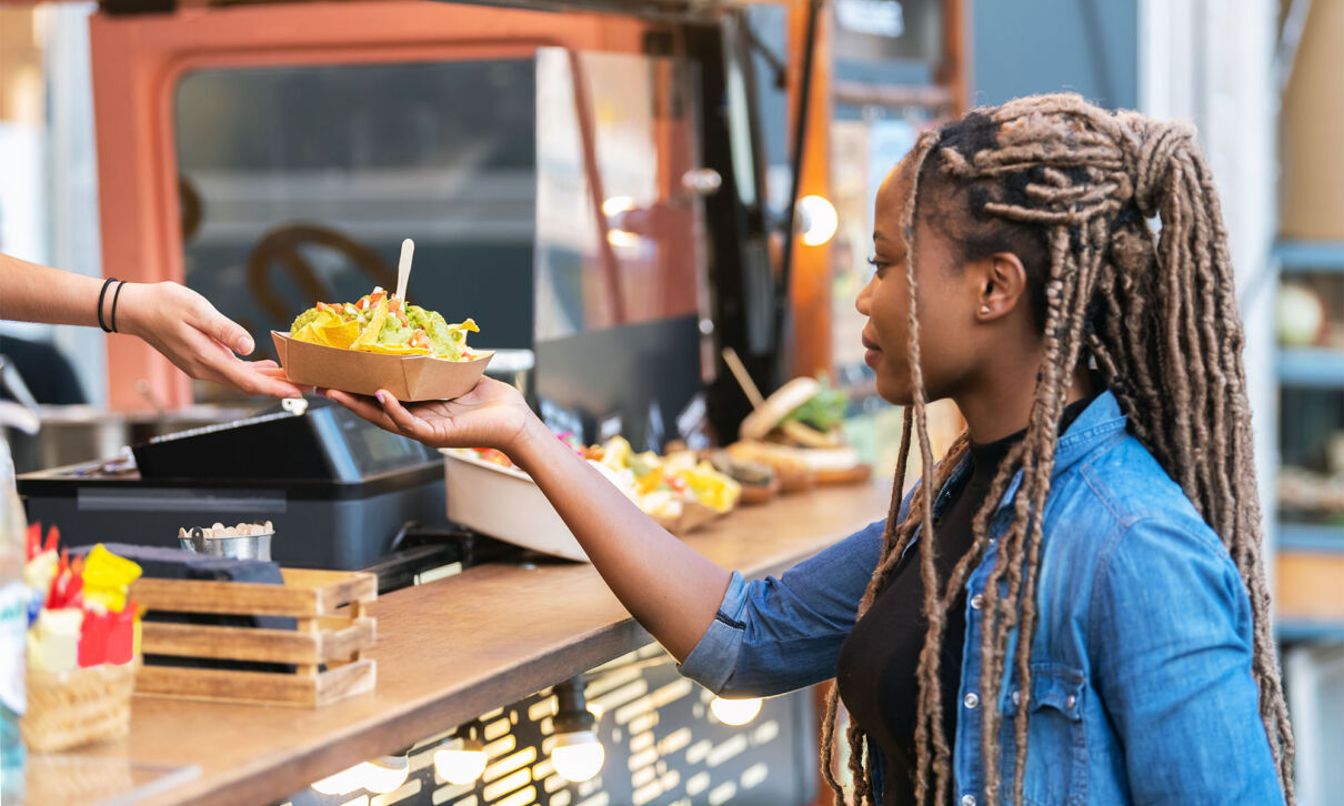 Eine Frau an einem Stand auf einem Street-Food-festival nimmt eine Speise in einer Schale entgegen