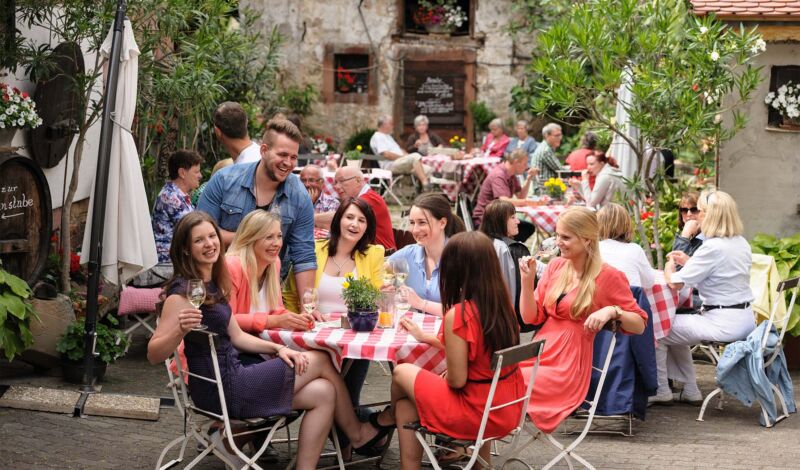 Besucher eines Weinfestes sitzen in einem Innenhof und trinken Wein