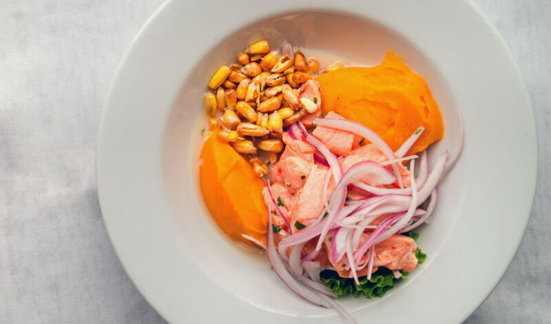 Peruanisches Gericht Ceviche mit Mais, Zwiebeln und Süßkartoffeln auf einem weißen Teller