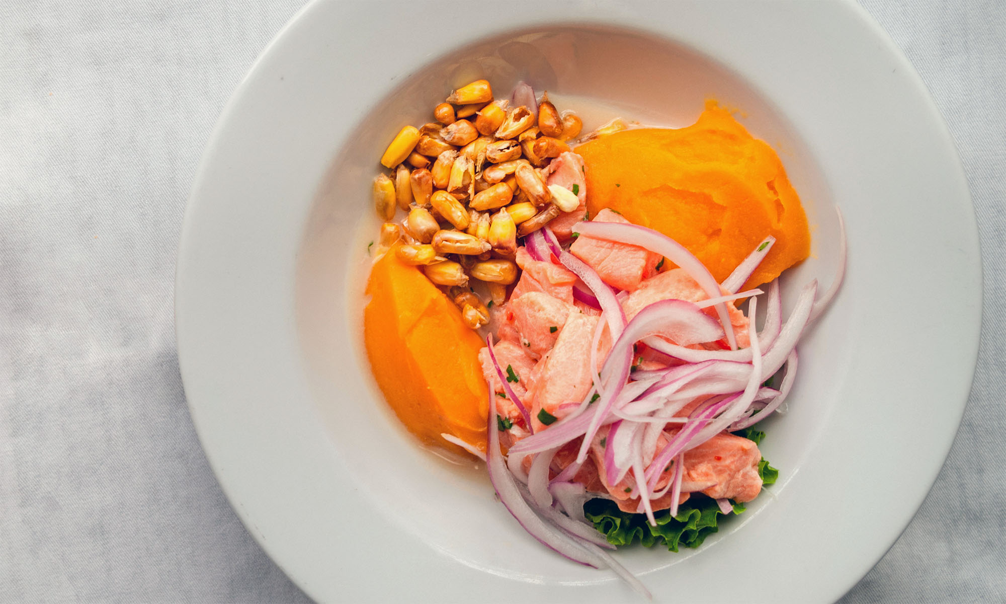 Peruanisches Gericht Ceviche mit Mais, Zwiebeln und Süßkartoffeln auf einem weißen Teller