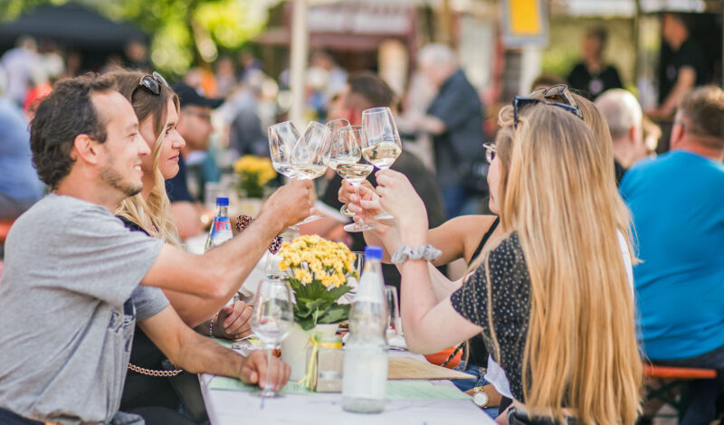 Mehrere Personen stoßen mit Weißwein auf einem Weinfest an.