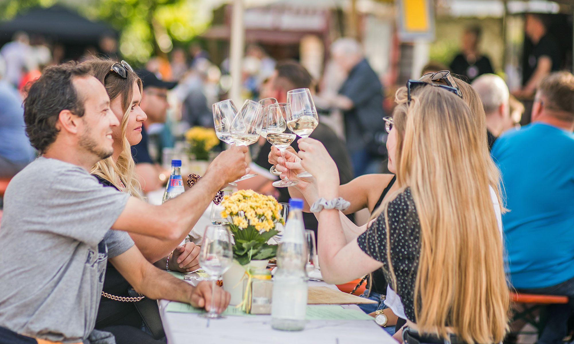 Mehrere Personen stoßen mit Weißwein auf einem Weinfest an.