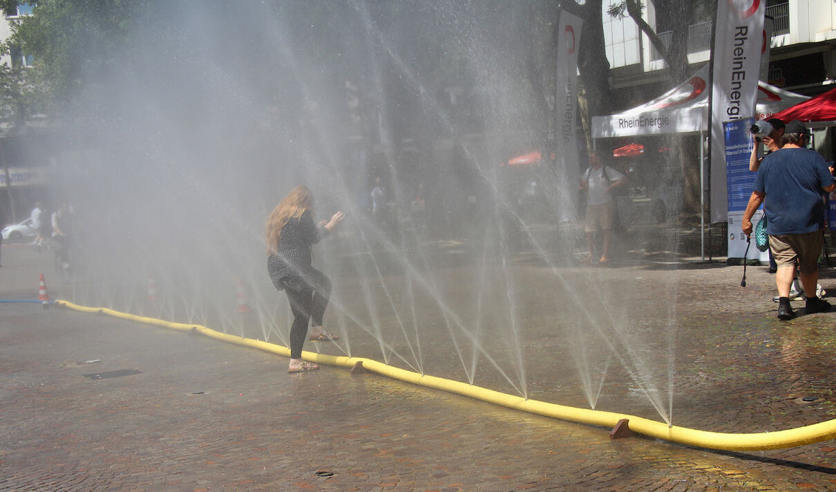 Eine Frau kühlt sich unter dem Sprühregen aus einem perforierten Feuerwehrschlauch ab.