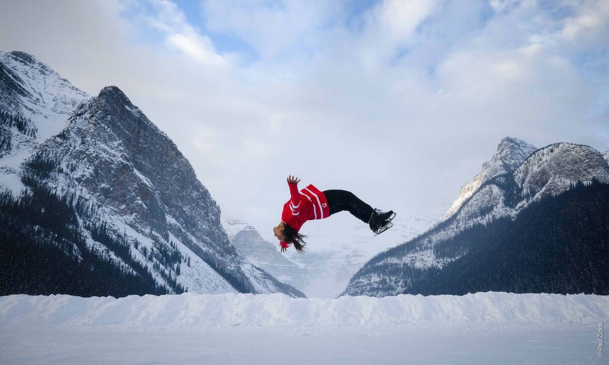 Eine Skispringerin mach vor winterlicher Bergkulitte einen Salto.