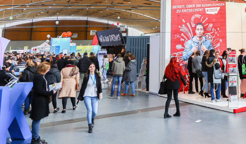 Besucher auf einer Jobmesse stehen an Ständen.
