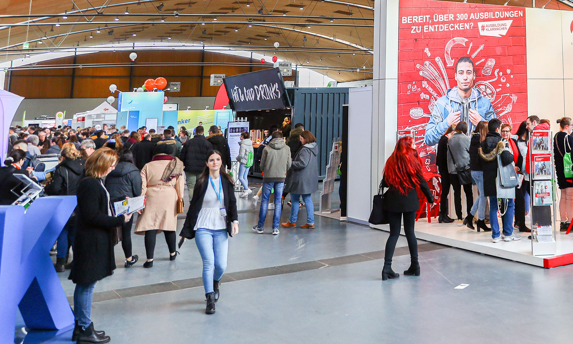 Besucher auf einer Jobmesse stehen an Ständen.