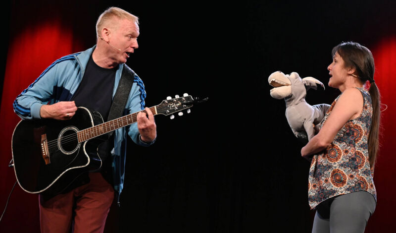 Zwei Schauspieler mit Gitarre und Esel-Handpuppe auf der Bühne.