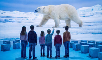 Kinder in der Ausstellung, die in einer Arktisszenerie stehend einen Eisbären betrachten.