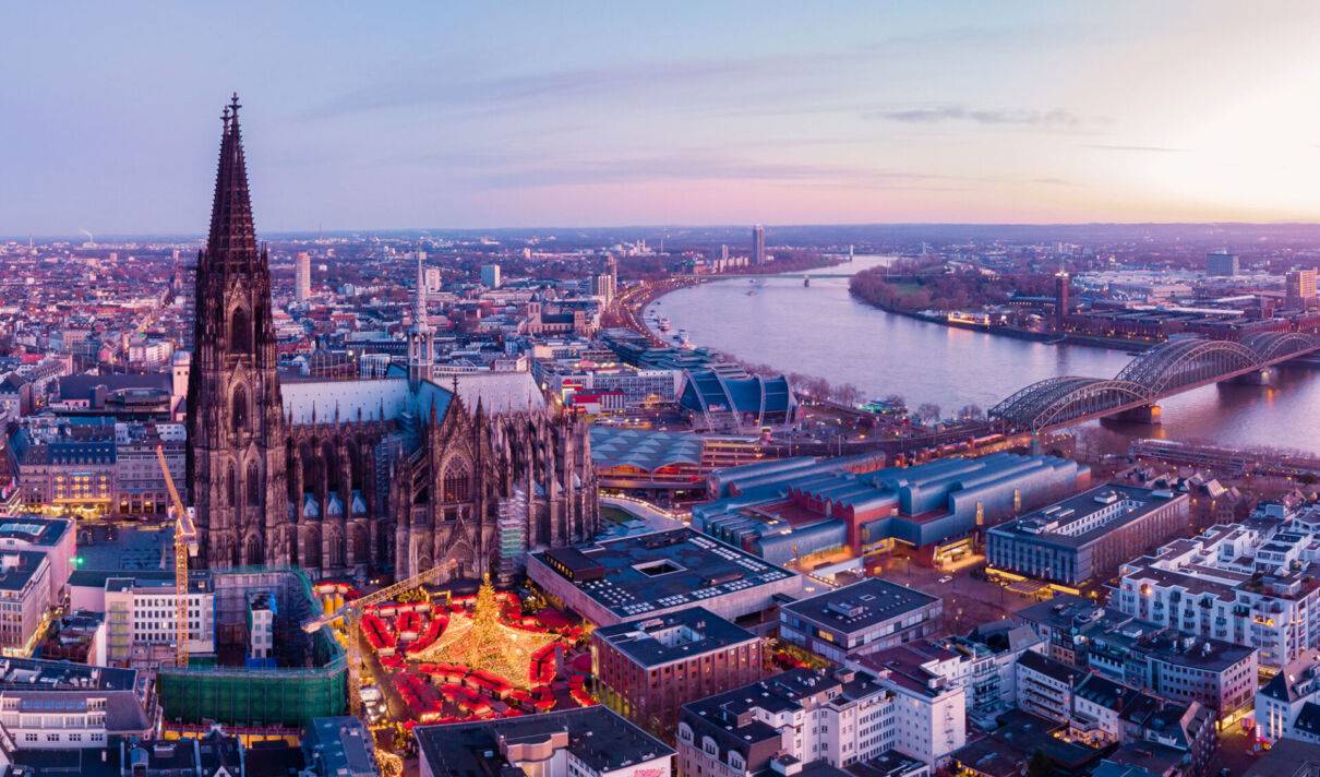Kölner Stadtpanorama in der Dämmerung, mit Weihnachtsmarkt vor dem Dom.