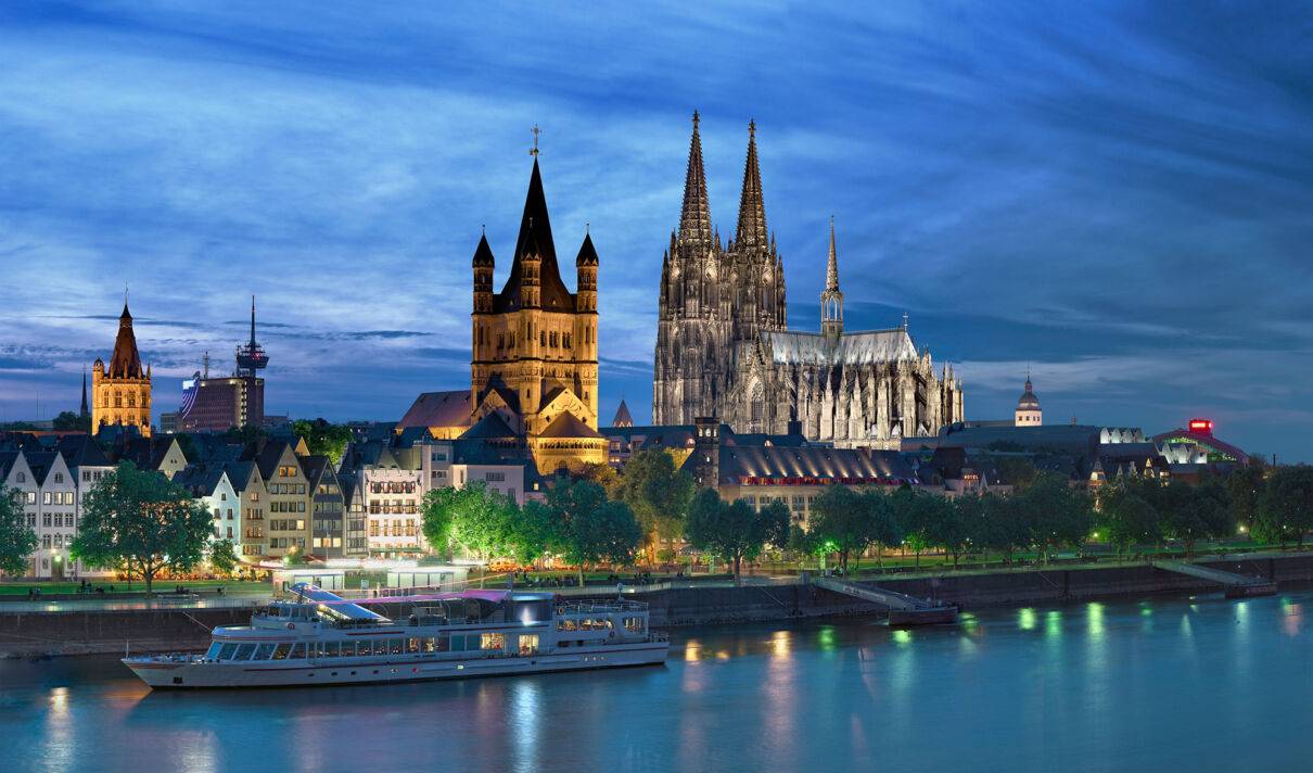 Foto des Kölner Rheinpanoramas bei Dämmerung mit beleuchtetem Dom und Groß St. Martin